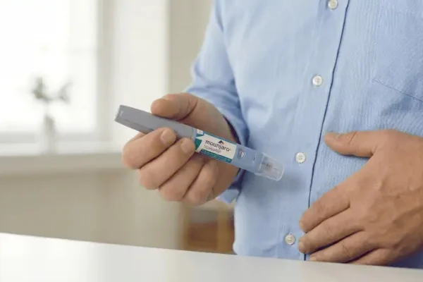 Persoon met een blauwoverhemd met een hand op de buik en in zijn andere hand houd de persoon een mounjaro pen vast